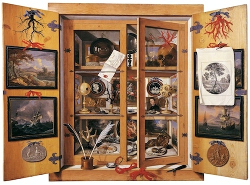 a wood and glass display cabinet colorfully filled with items such as small paintings, etchings, coral, feathers, mirrors, a skull, etc.