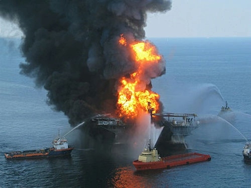 aerial photo of the oil rig with huge flames and billowing black smoke, surrounded by fireboats shooting streams of water at the conflagration