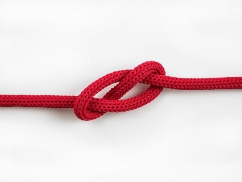 close-up photo of a simple red rope tied in a loose overhand knot against a plain white background