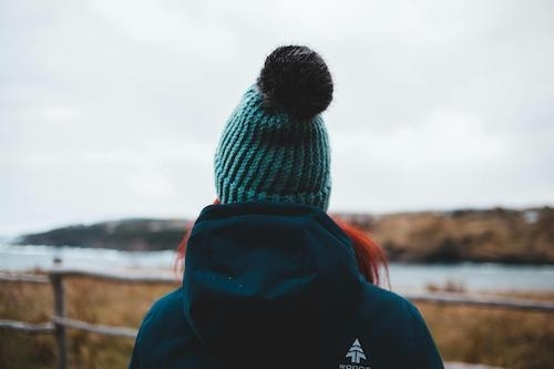 view from behind of an anonymous traveler in beanie hat and warm clothes admiring countryside river in fall