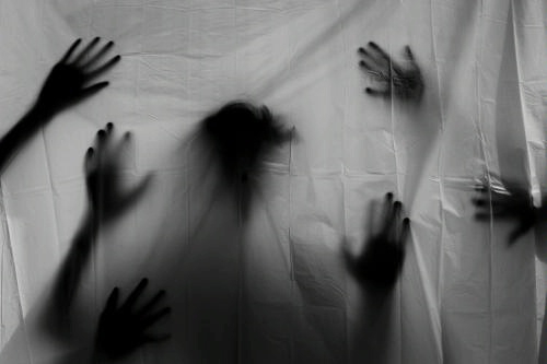 Photo via pixabay.com: black and white photo of spooky silhouetted figure behind a sheet, with many hands reaching out toward the viewer