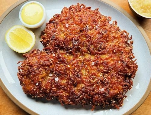 Author's photo of a schnitzel latkes on a white plate with a sliced lemon 