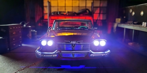 photo of a dark and colorful miniature focusing on a beautiful but menacing, glossy, vintage red Plymouth Fury with its lights on inside a dark scruffy garage space 