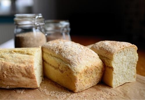 on a table against a dark background, 2 loaves of bread cut in half and one whole loaf