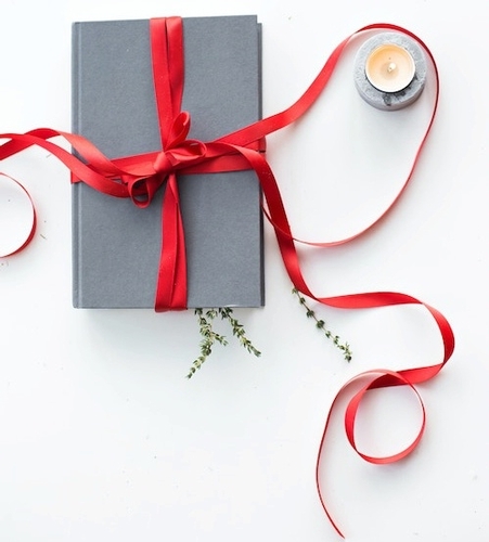 Gray book wrapped with red ribbon beside a tea candle