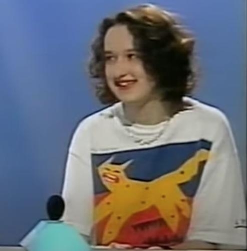 girl on a game show wearing a white t-shirt with a bright screen-printed design showing a stylized yellow feline against a blue and red background