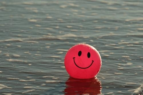 photo of a large orange-red ball with a happy face floating on sparkling water