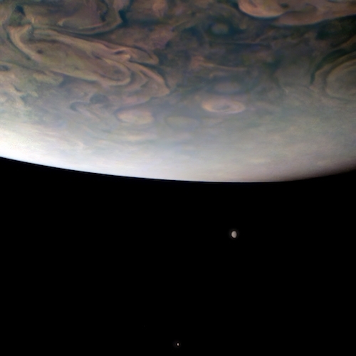 With a partial image of Jupiter huge in the top foreground, we see two two small moons in black space below it
