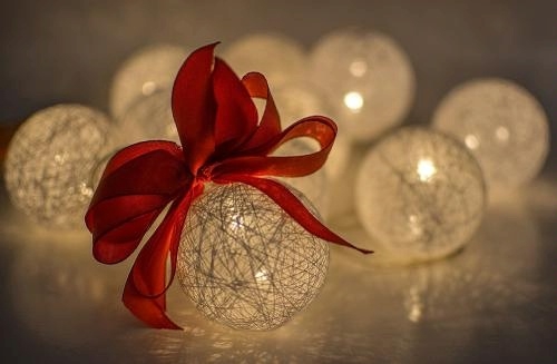 moody, cozy image of glowing white etched ball ornaments and a red ribbon bow