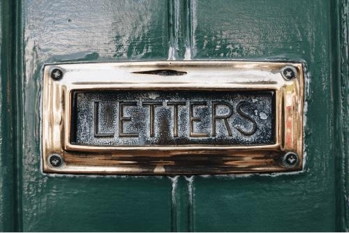 close-up photo of the front of an old fashioned mail slot in a door, with the word  LETTERS embossed on the metal flap