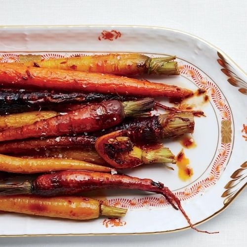 photo of delicious looking roasted, slightly charred slender whole carrots in hues of orange and yellow on an elegant china serving plate