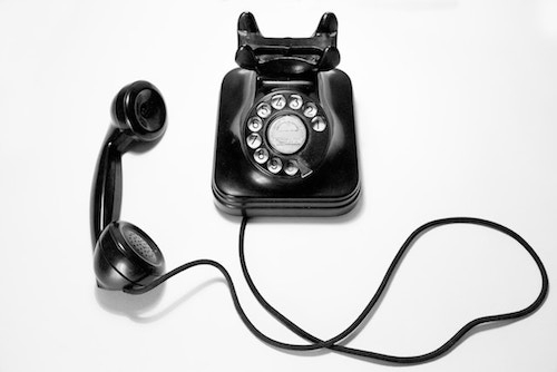 Old fashioned black rotary dial phone on white surface