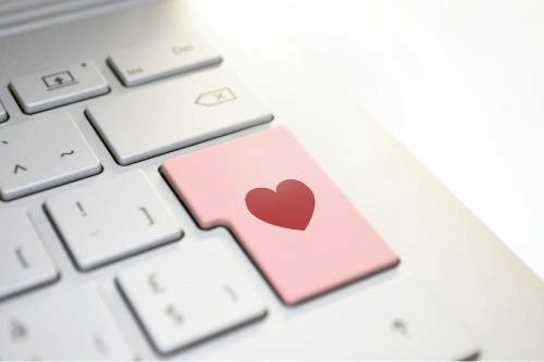 image via pixabay.com: a close-up of a white computer keyboard, with one key prominently. The key is colored pink and has a red heart symbol on it, standing out from the other white keys. The heart symbol on the key suggests a theme of love or affection related to technology or communication.