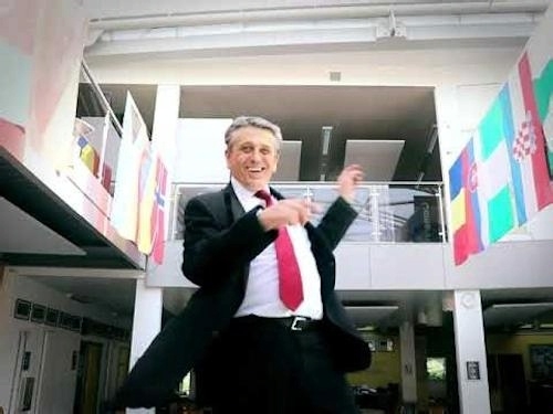 Youtube screenshot of Mr Ferry, a broadly smiling white man with gray hair probably in his 50s, wearing a suit and tie, dancing in a school setting