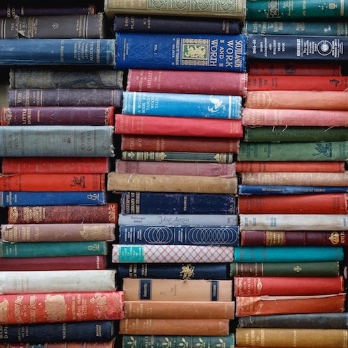 Three tall stacks of old and vintage books, spines facing front, with different, colorful bindings and covers.
