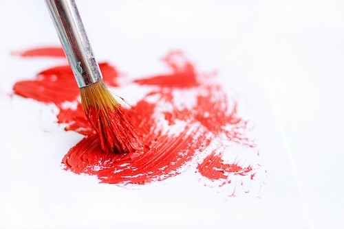 photo close-up of the tip of a paintbrush brushing salmon colored paint on a white surface