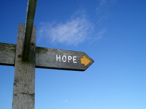  A wooden crosspost sign with the word HOPE and an arrow pointing right against a bright blue sky
