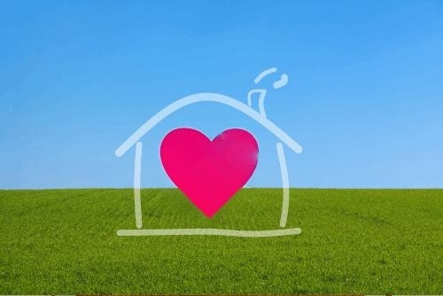 red heart inside the white outline of a simple house against a green grass and blue sky background