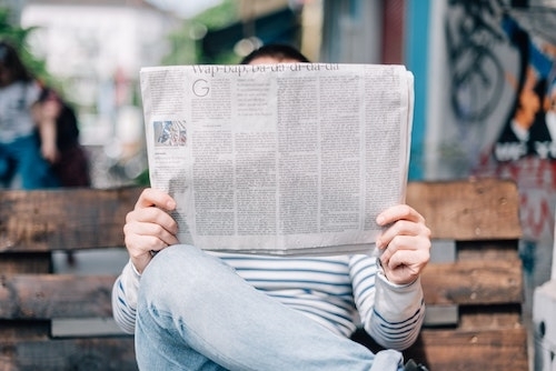 Photo by Roman Kraft on unsplash.com: a man in jeans sitting on an outdoor bench reading a newspaper