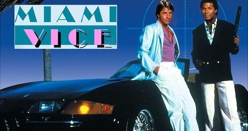 promotional image featuring the Miami Vice logo and a nighttime shot of Crockett and Tubbs looking stylish next to a Ferrari Daytona Spyder