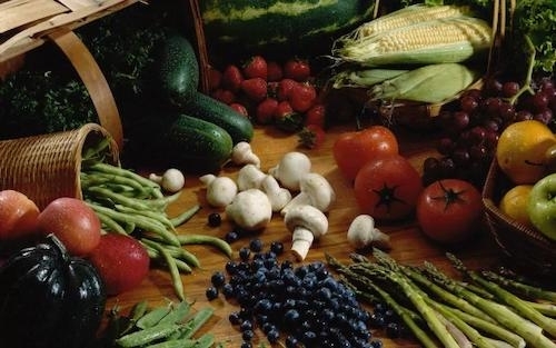 A colorful still life photo of a variety of fruits and vegetables arranged on a wooden tabletop