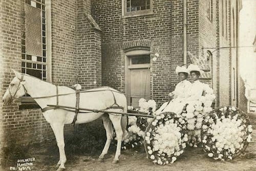 vintage photo of two African American women dressed all in white with white hats in a white cart decorated with flowers and pulled by a white horse