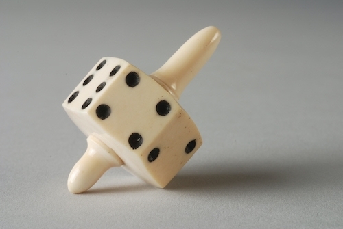 photo of a teetotum, an ivory device similar to a top, with a 6-sided die on a spindle for spinning.