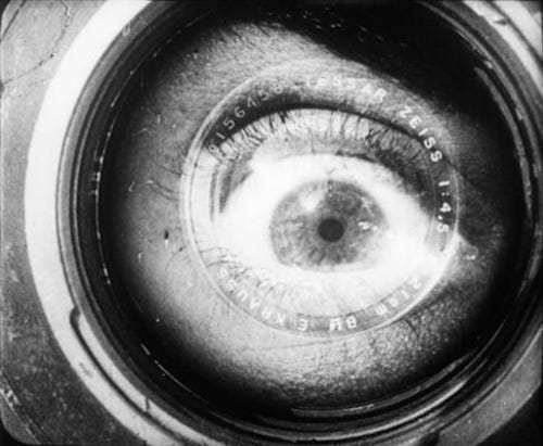 close-up of a wild-looking wide open human eye peering through a camera lens
