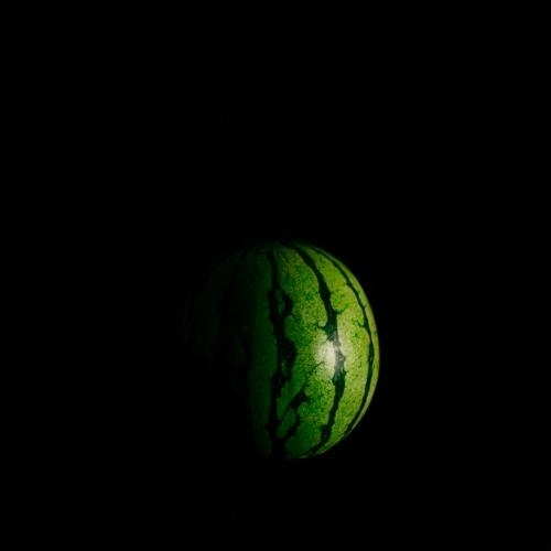 dark photo of a whole watermelon with light shining on it from right, making it look like a moon or planet in space