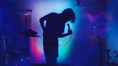 moody silhouette photo of Bo Burnham onstage speaking into handheld mic