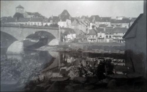 old black and white photo of a 1940s French village on a river or canal with a prominent bridge visible