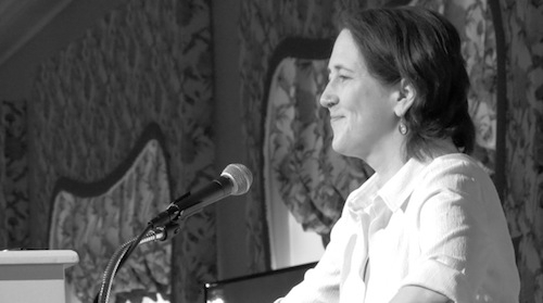 black and white side view photo of Jessamyn smiling in white blouse seated in front of microphone